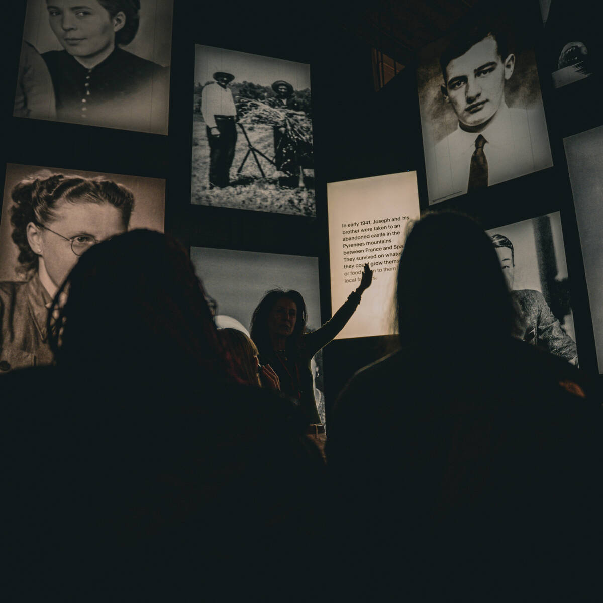 A tour guide pointing out a quote on a fall flanked by large images of faces in black and white with the tour group in the foreground.